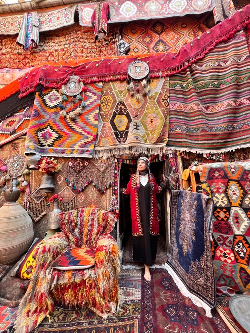 Free A woman in traditional attire stands in a vibrant Turkish carpet shop filled with colorful textiles. Stock Photo