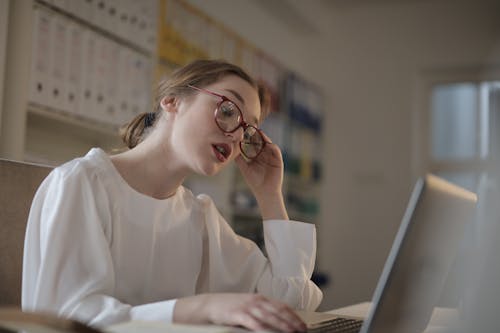 Woman In White Long Sleeve Shirt Wearing Eyeglasses Using A Laptop Computer