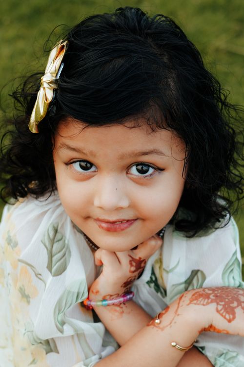 Free Adorable portrait of a young girl with henna on her hands, wearing a floral dress, outdoors. Stock Photo