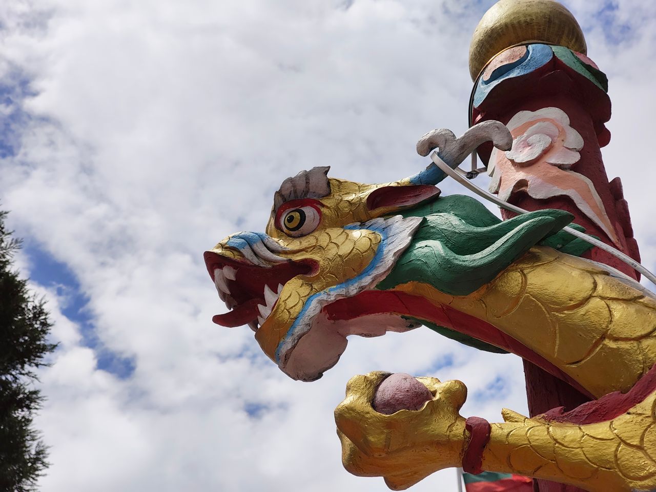 boldly colored chinese dragon sculpture against a cloudy sky displayin