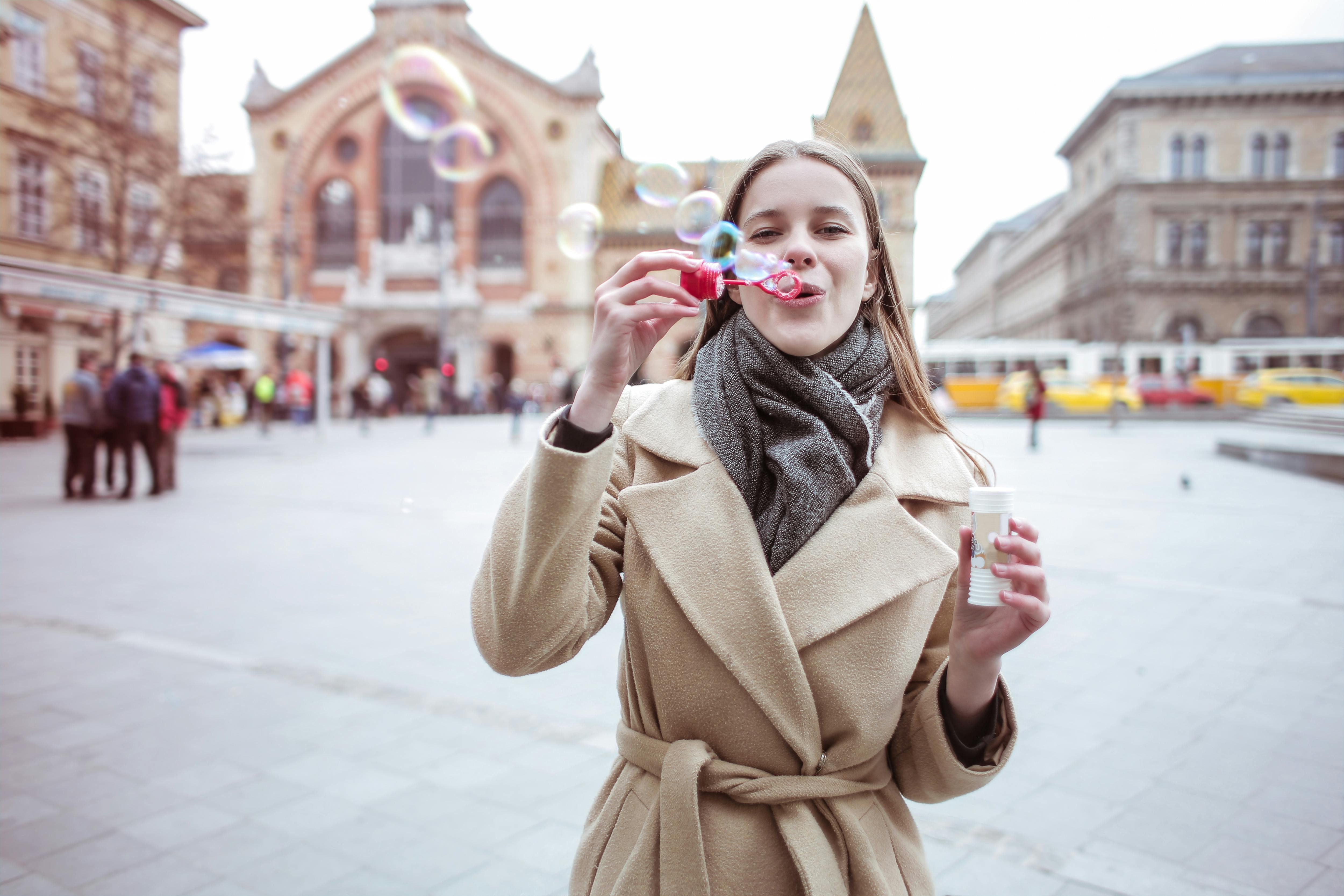 A young woman joyfully blows bubbles in a winter city square, surrounded by historic architecture.