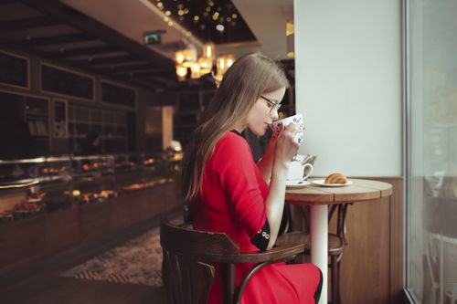 Free A woman in a red dress enjoys coffee inside a cozy café. Stock Photo