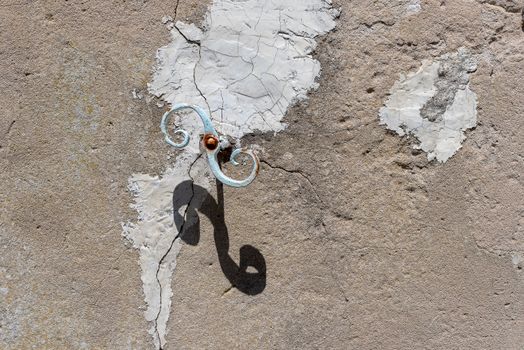 Rusted metal hook casts a shadow on a textured, cracked wall. Artistic and abstract.