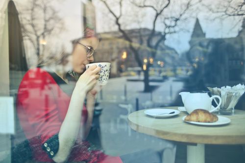 Free Woman enjoying a cup of coffee in a cozy cafe setting, viewed through window reflection. Stock Photo