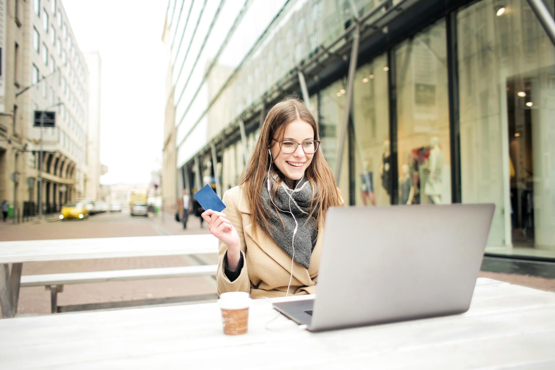 Businesswoman smiling while using laptop and holding credit card outdoors.