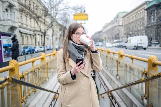 城市街道上，一位冬季时尚的女性边喝咖啡边使用智能手机