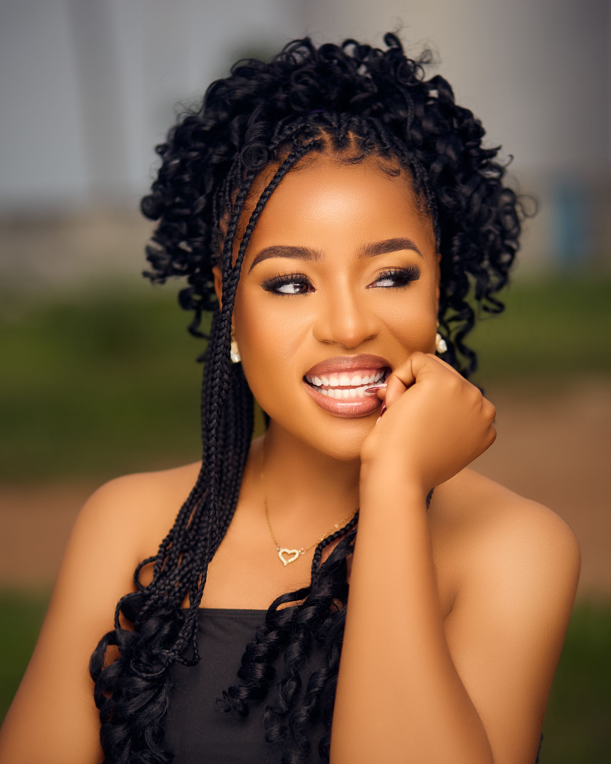 Portrait of a smiling woman with braided hair outdoors, exuding joy.