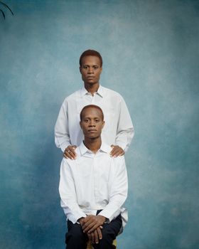 Studio portrait of two men in white shirts against a blue background.