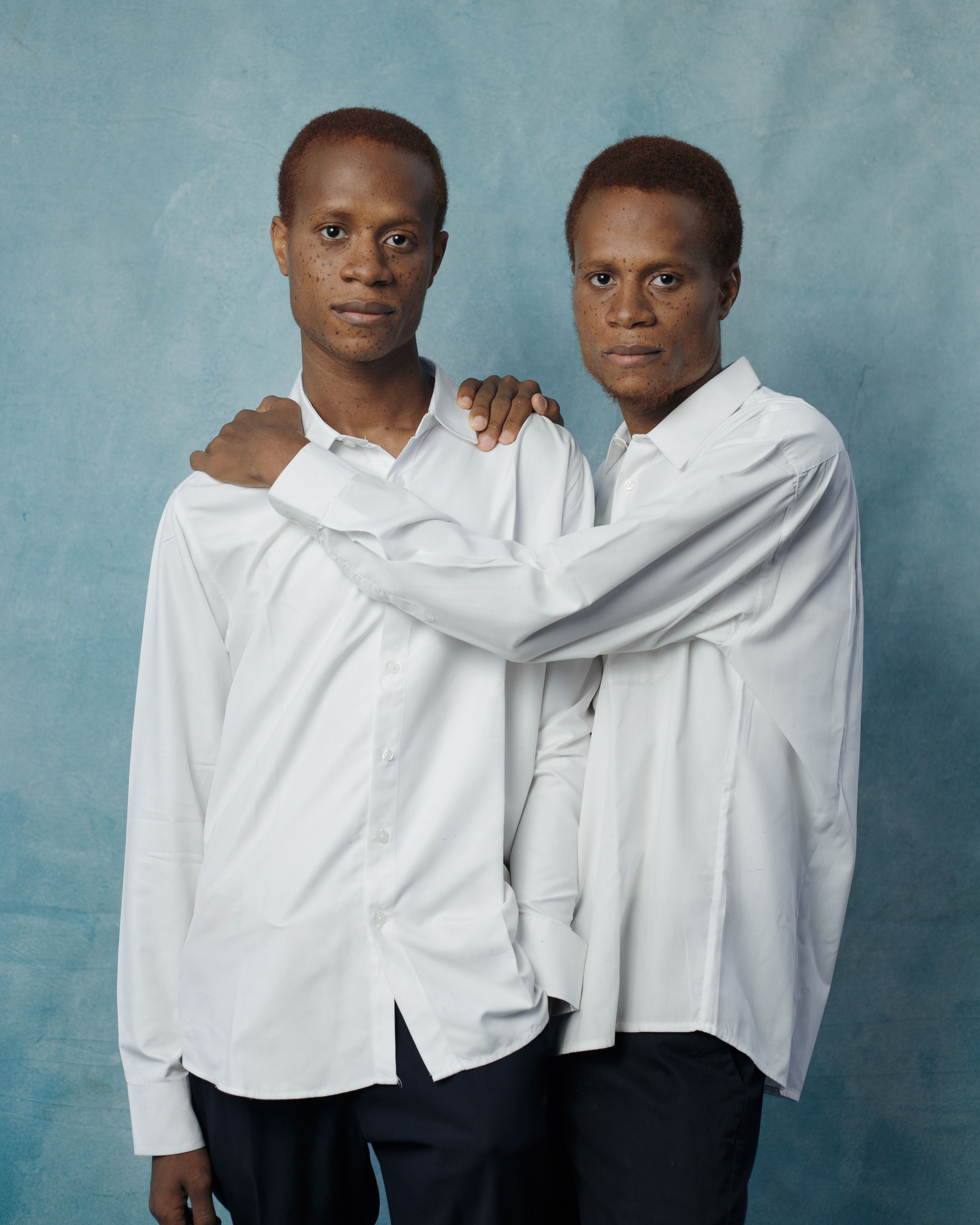 Twin brothers wearing white shirts pose against a blue backdrop, exuding unity and style.