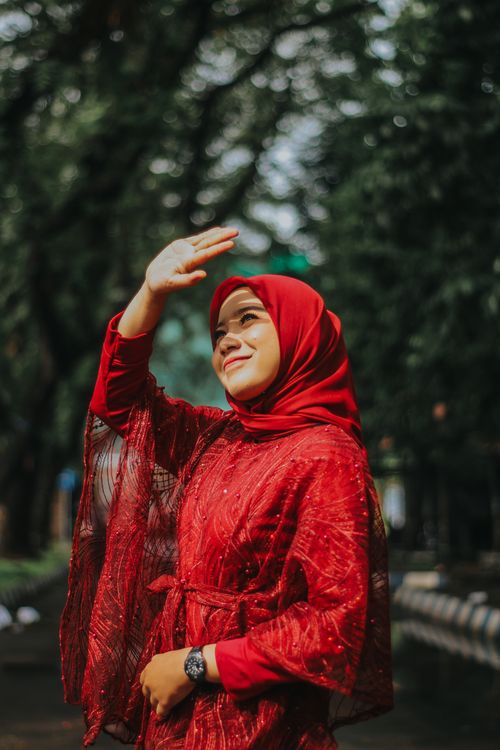 Free A joyful woman wearing a red hijab enjoying the sunshine in a lush park setting. Stock Photo