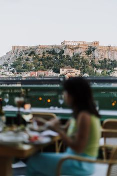 A woman dining outdoors with a scenic view of the Acropolis in Athens, Greece.