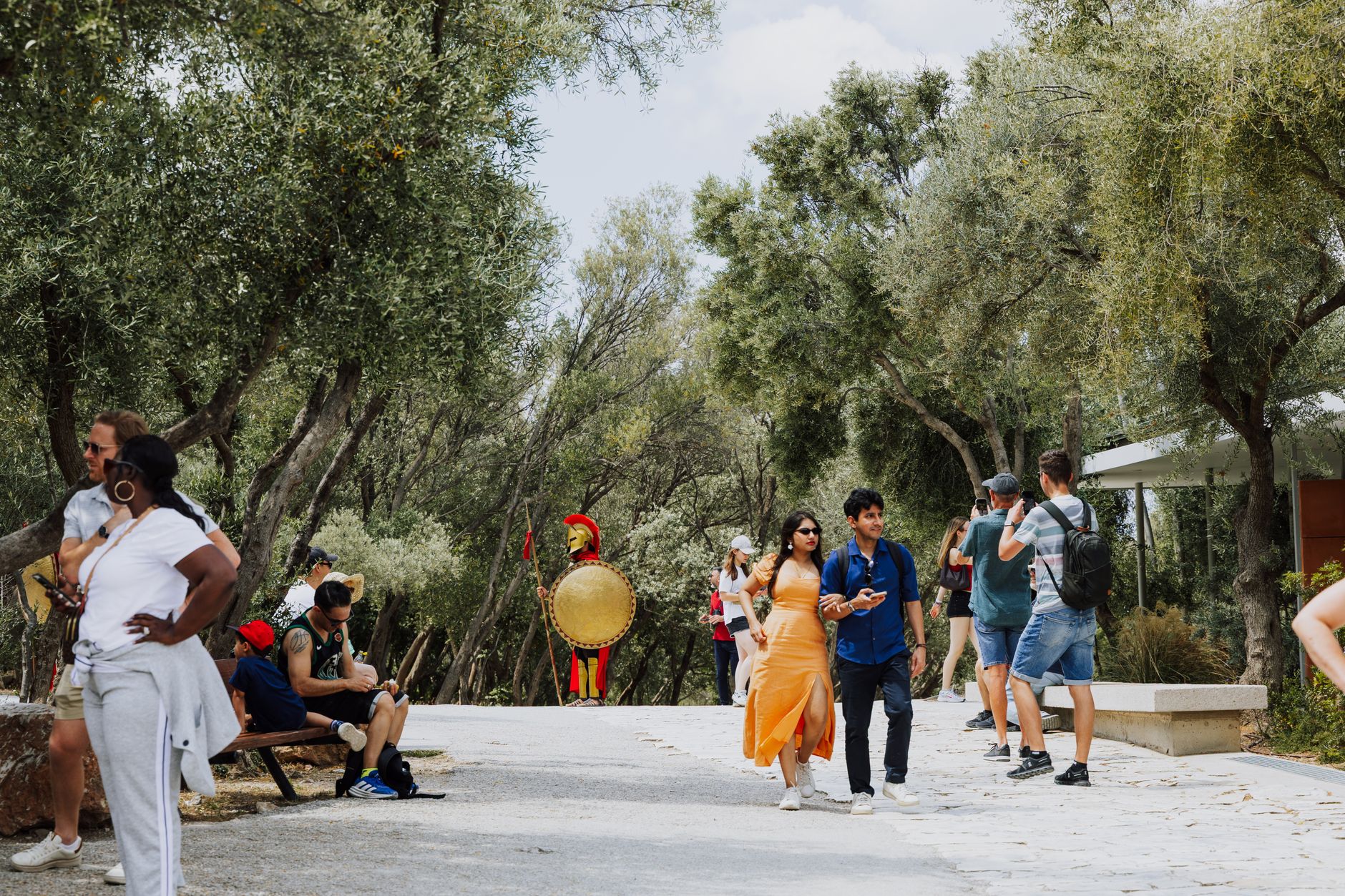 Visitors enjoy a scenic walk through a historic park in Athens, Greece, featuring lush trees.