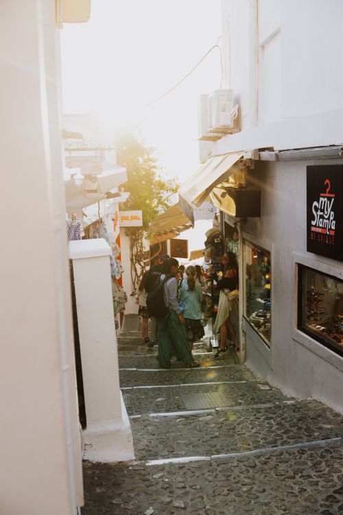 Free Charming sunlit street in Fira, Greece with people shopping and exploring the local shops. Stock Photo