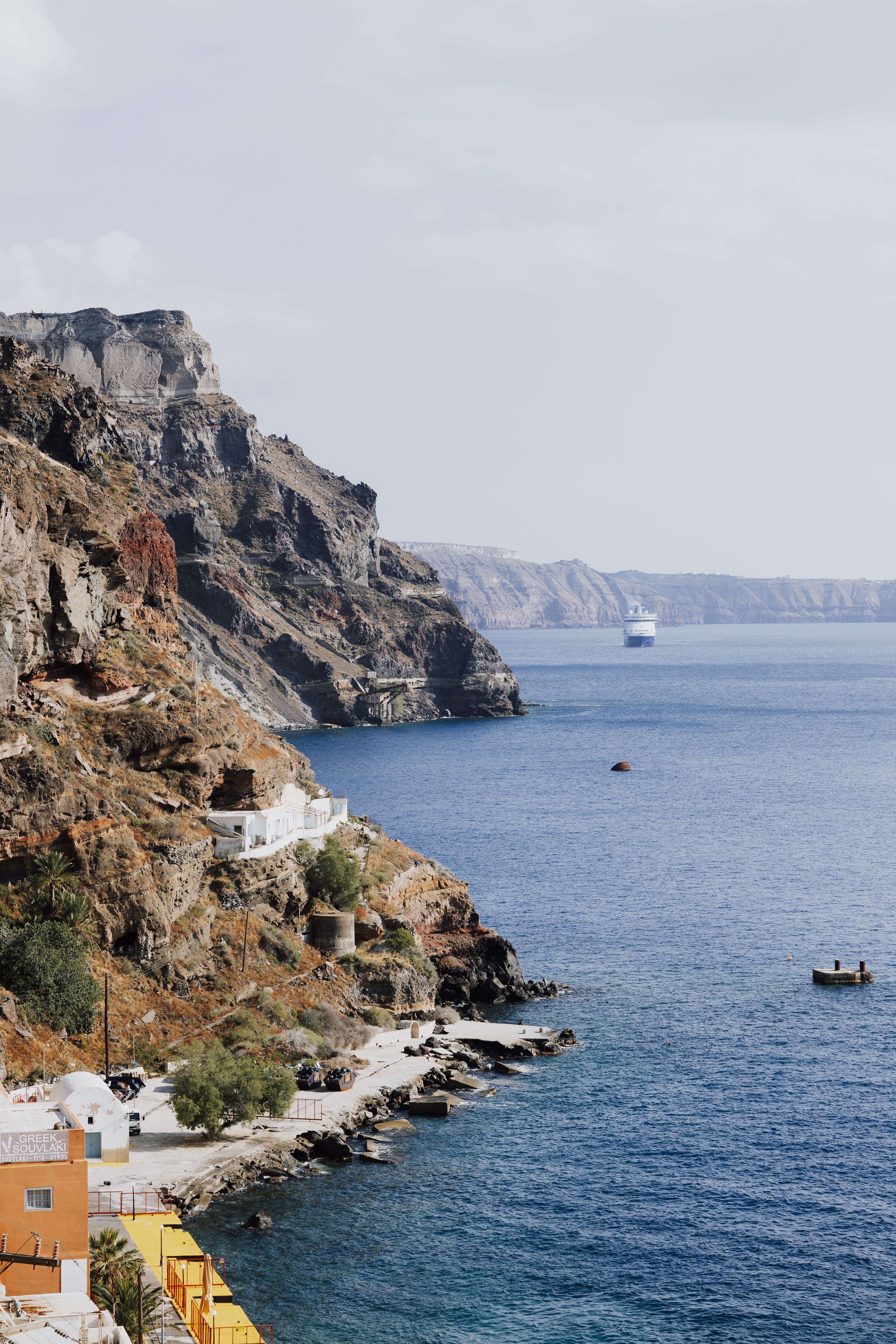 Breathtaking view of Fira's coastline in Greece with cliffs and a cruise ship on the horizon.