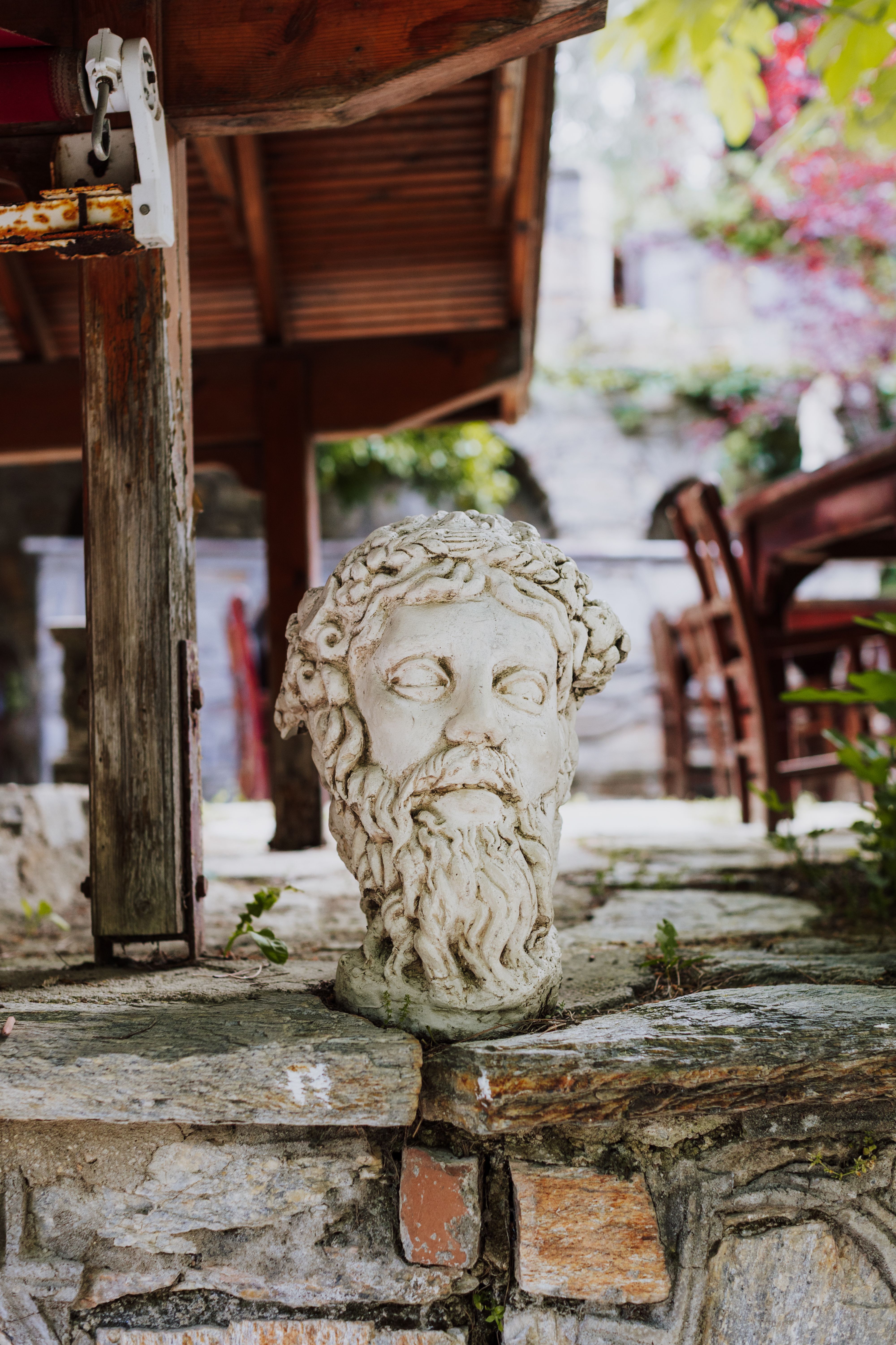 Ancient marble bust displayed outdoors under a pergola in İzmir, Türkiye, surrounded by lush greenery.