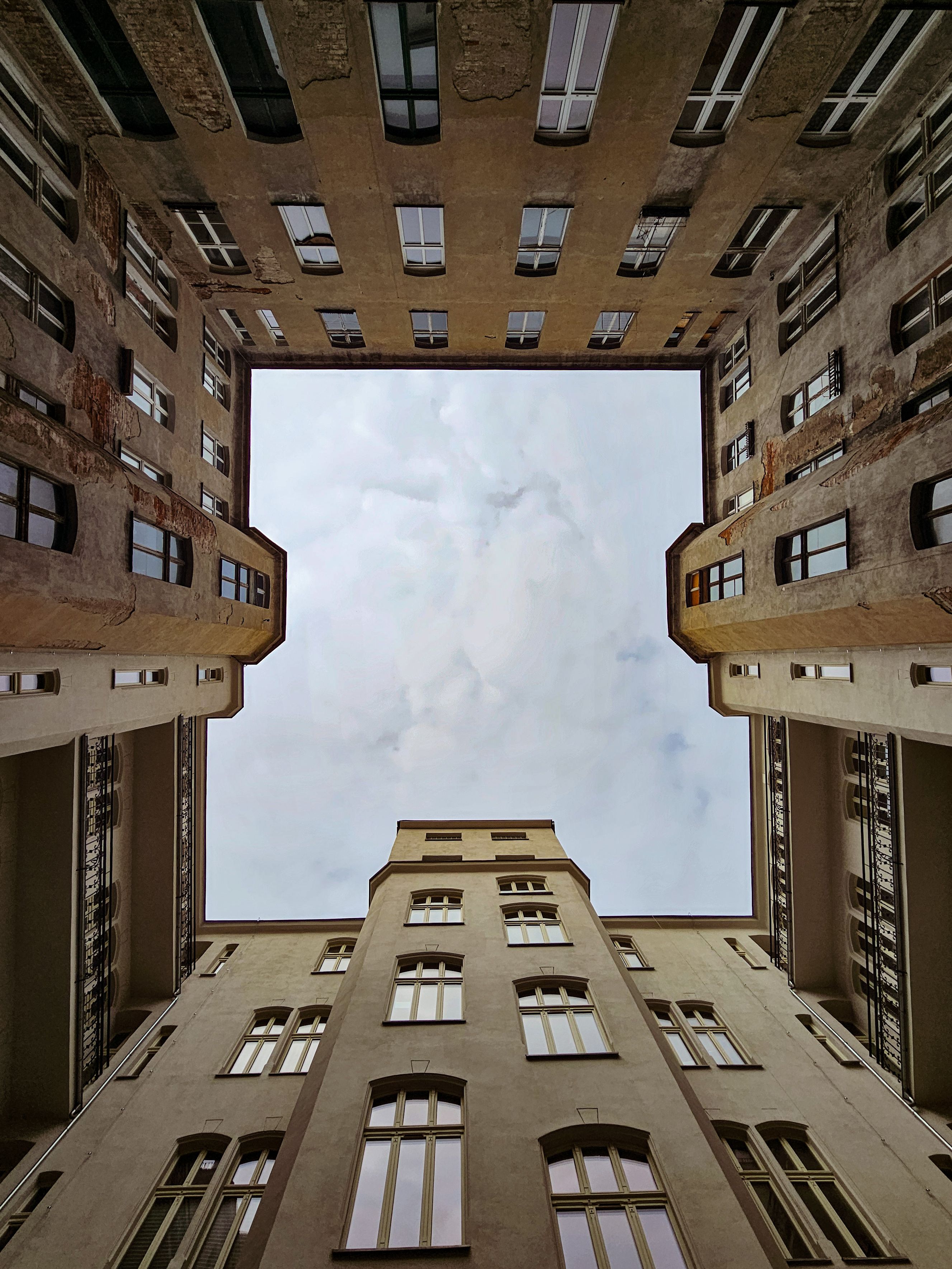 Upward view of a symmetrical urban courtyard framed by tall buildings under a cloudy sky.