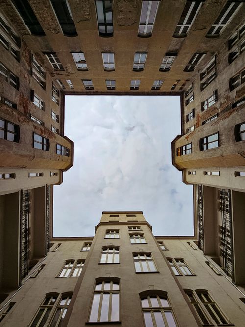 Free Upward view of a symmetrical urban courtyard framed by tall buildings under a cloudy sky. Stock Photo