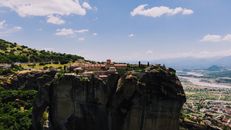 Breathtaking aerial view of the cliff-top monastery of Meteora in Greece, surrounded by lush landscapes.