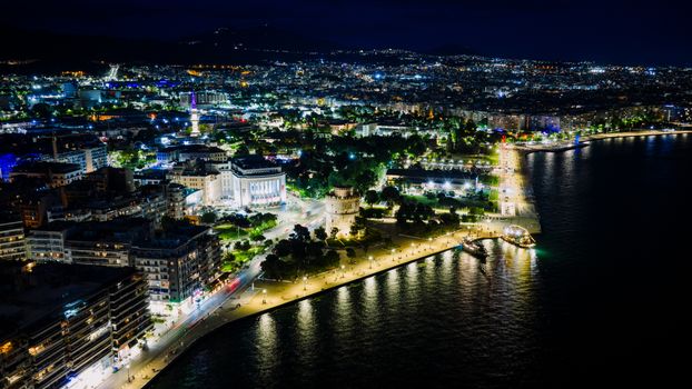 Abendliche Promenade von Thessaloniki mit beleuchtetem Weißen Turm und Menschen, die am Wasser spazieren gehen