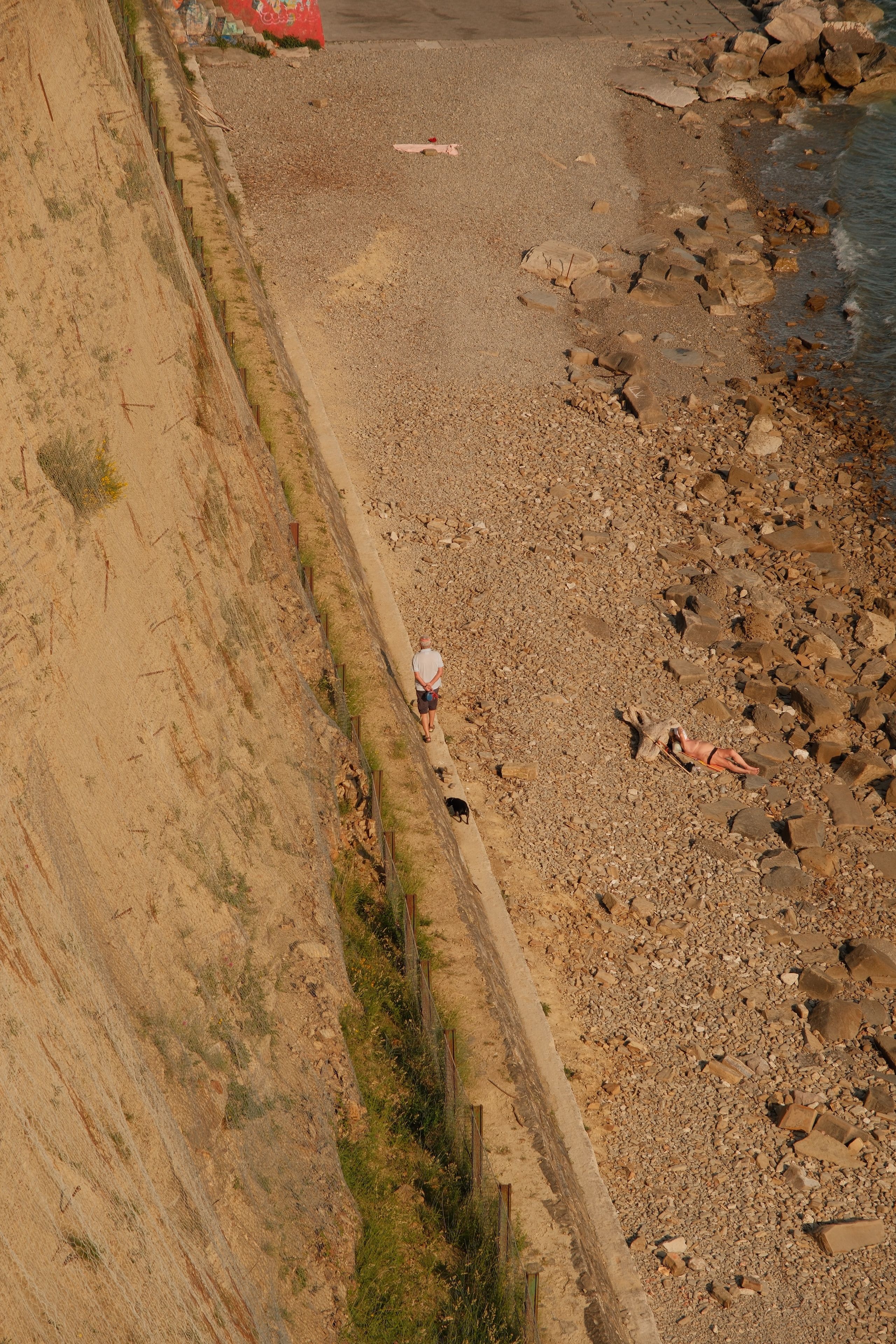 High-angle view of a rocky beach with people enjoying a sunny day by the sea.