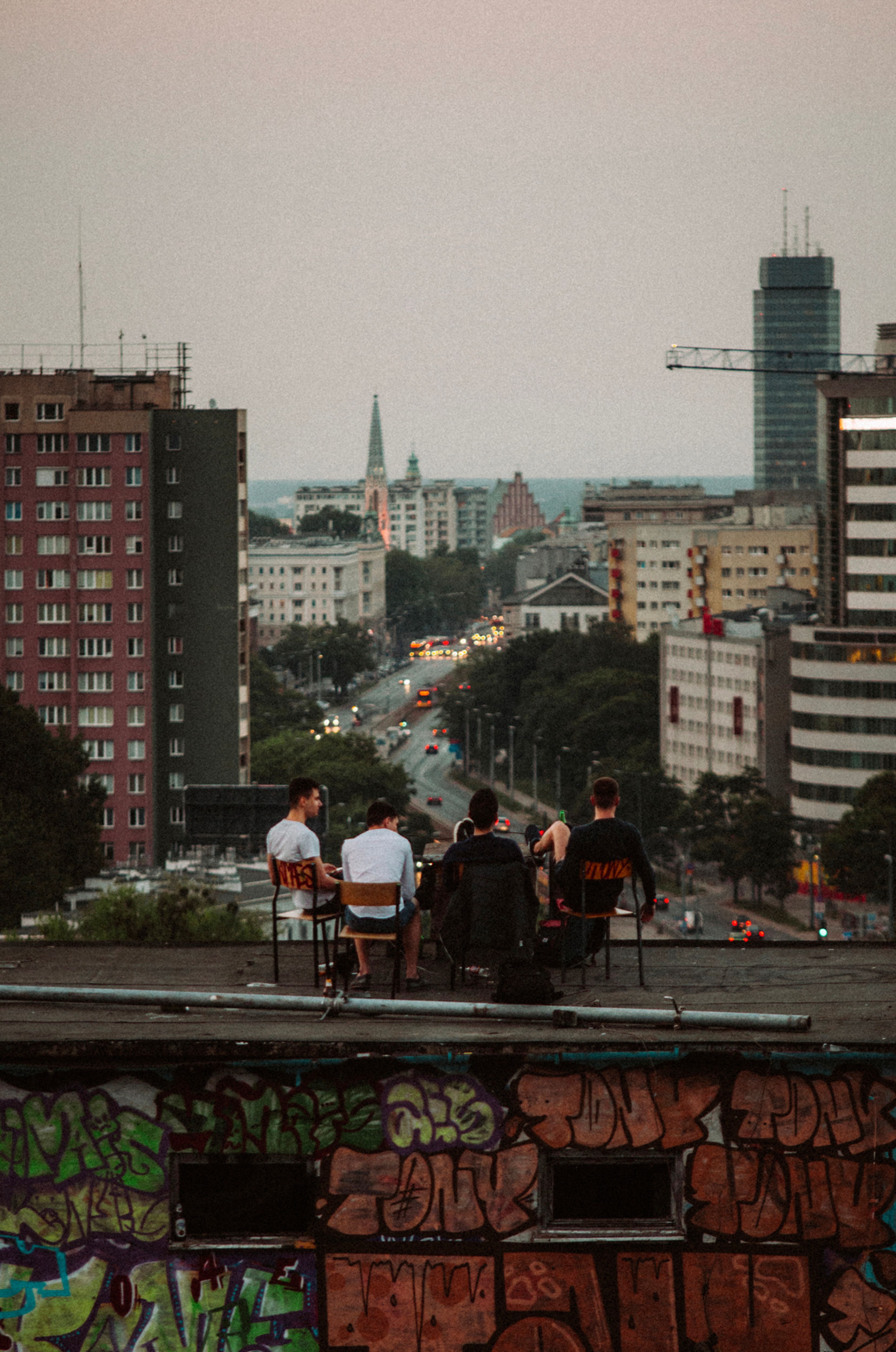 A group of people sitting on a rooftop with a cityscape view at dusk, urban atmosphere.