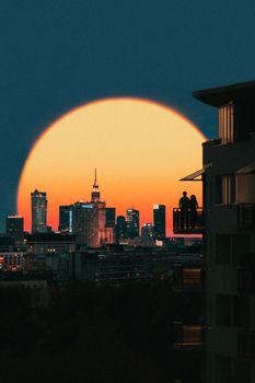 Silhouetted couple on a balcony watching a dramatic sunset over a city skyline.