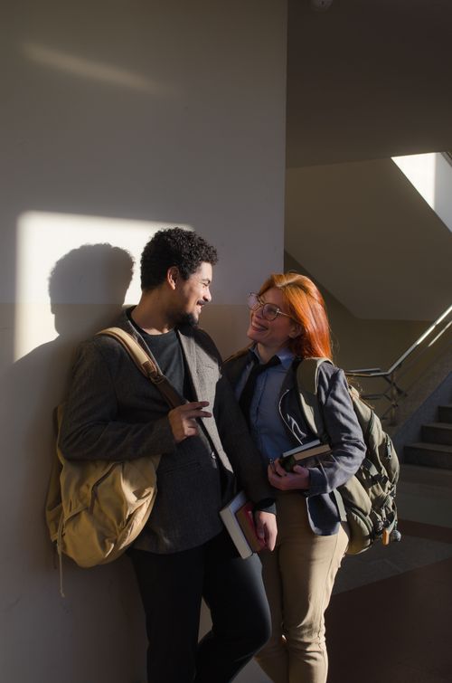 Free Two students chatting in a sunlit hallway, blending study and leisure. Stock Photo