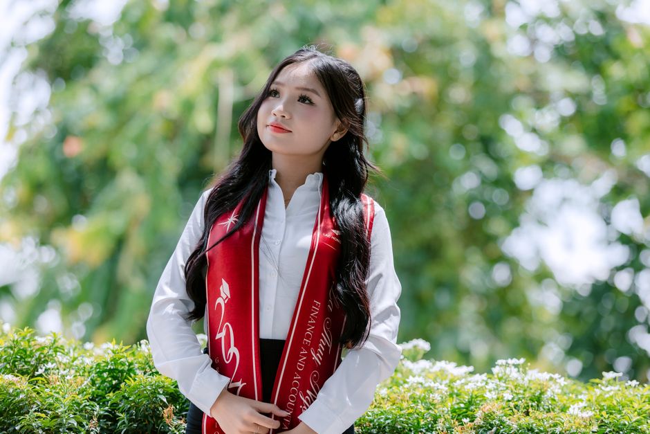 卒業式の衣装を着た若い女性が、屋外でポーズをとり、自身の功績を祝っている。