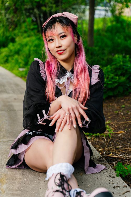 Free A woman elegantly dressed in Gothic Lolita fashion sits outdoors, surrounded by lush greenery. Stock Photo