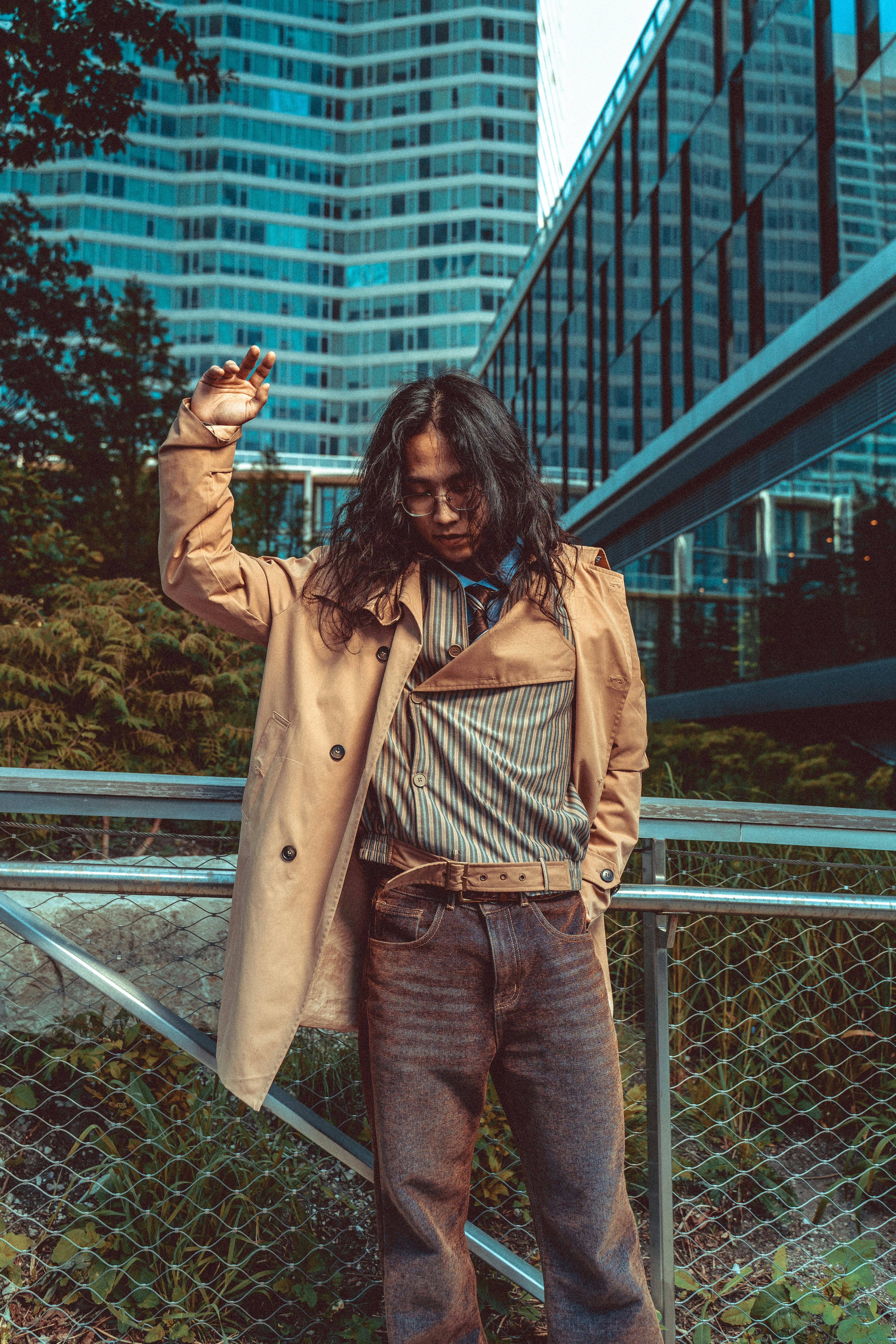 Fashionable individual posing in a modern urban setting with skyscrapers.