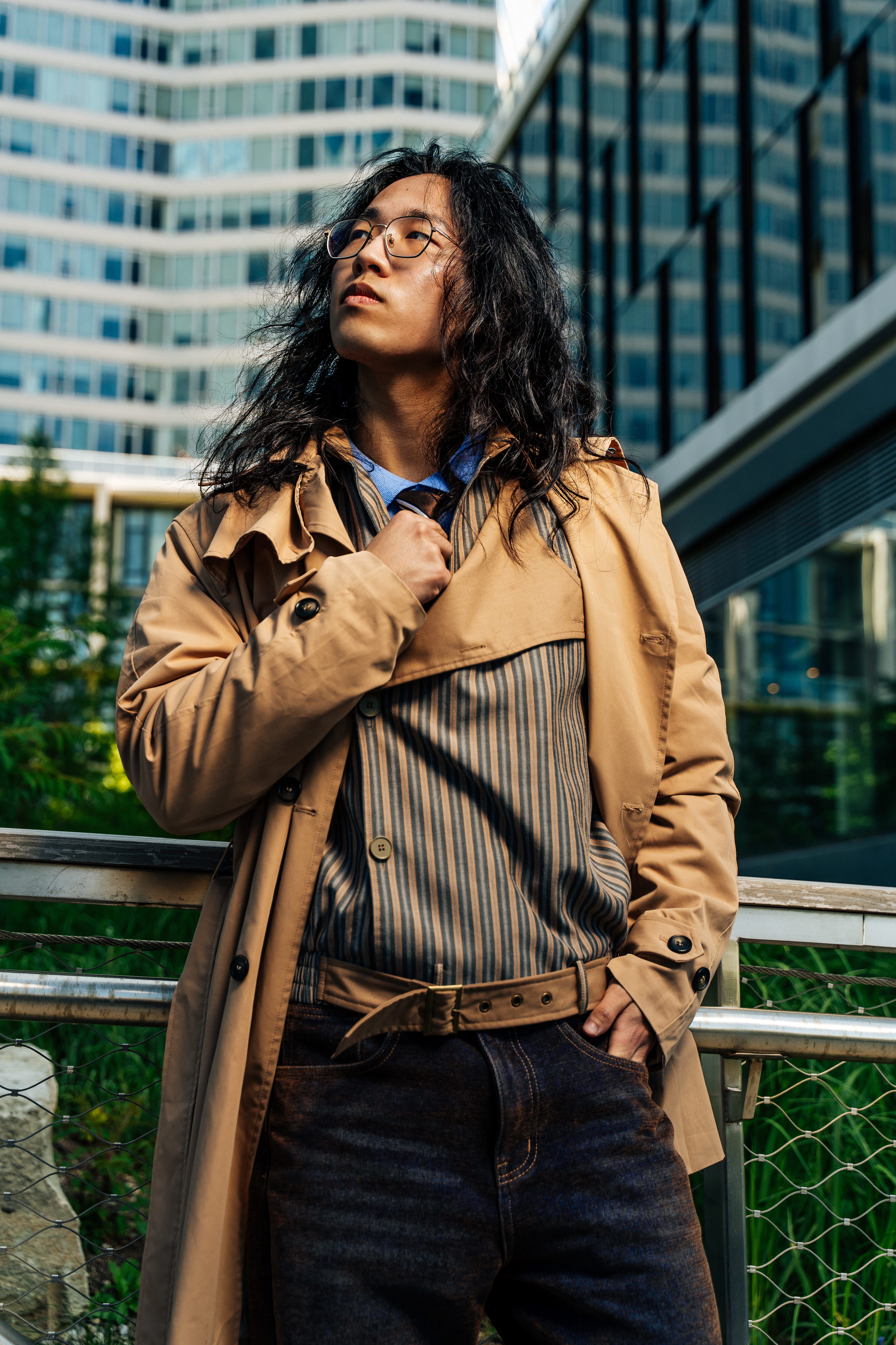 Young adult male in a trench coat confidently poses in a city setting.