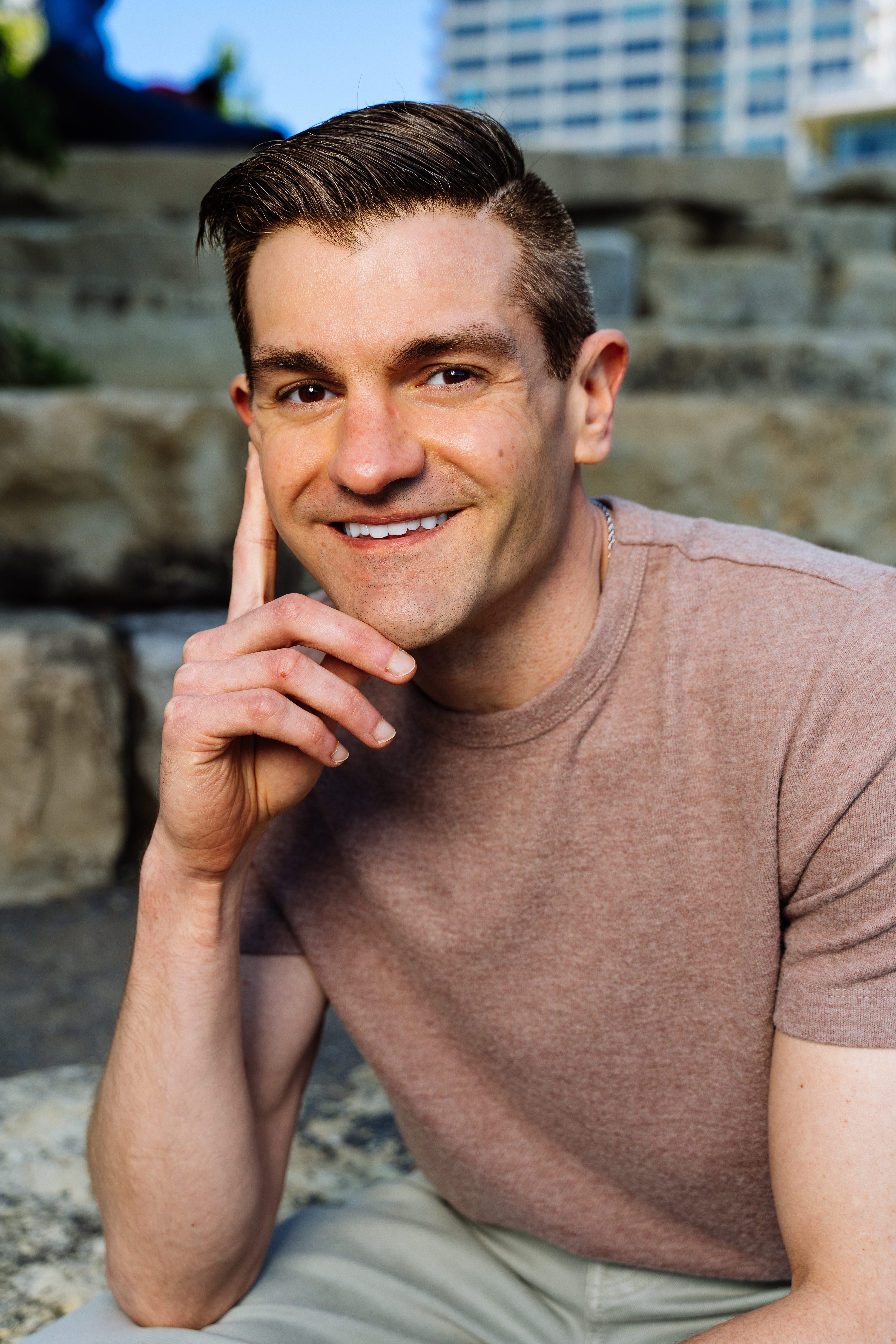 A relaxed outdoor portrait of a smiling man sitting on steps, showcasing natural lighting and casual attire.