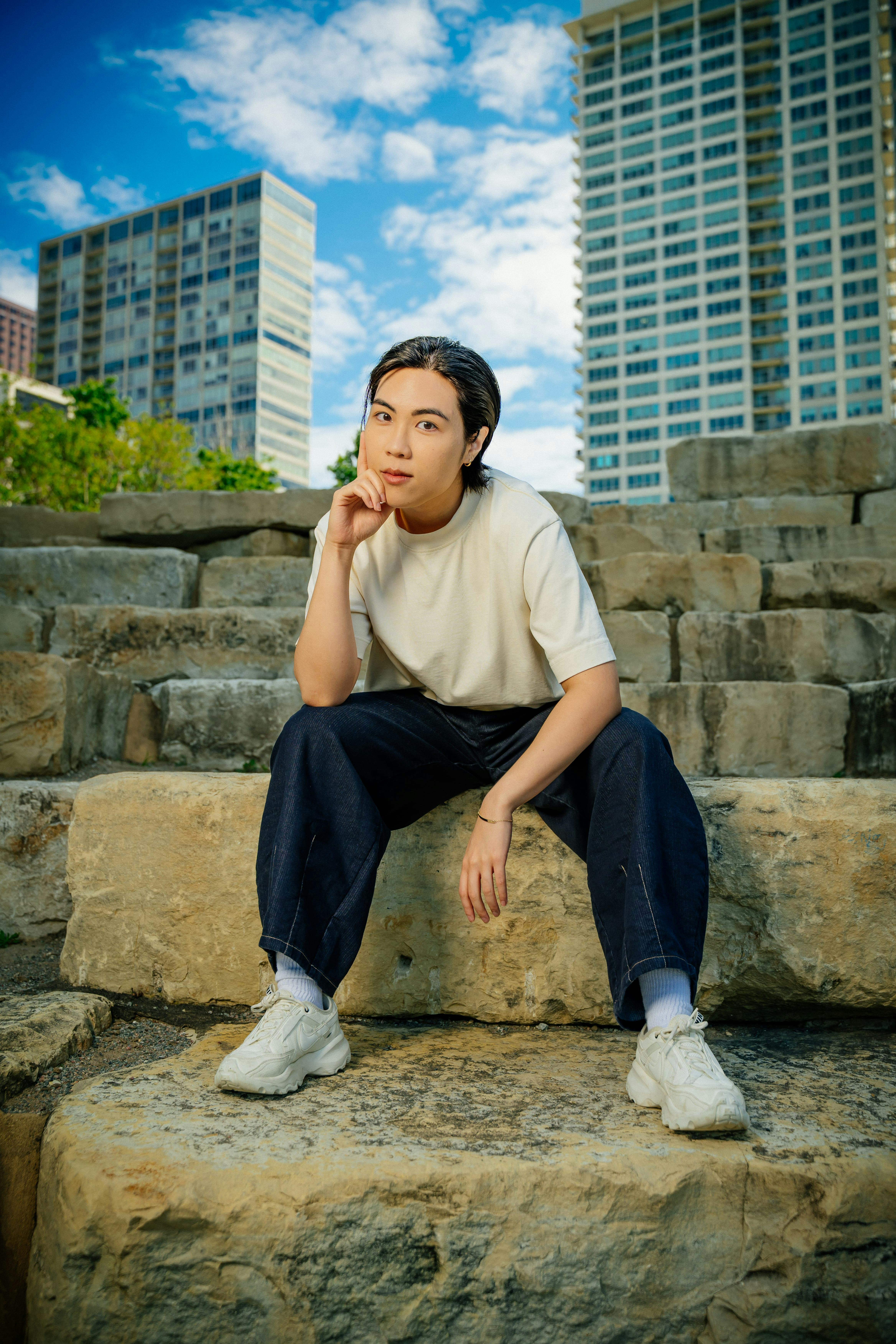 Fashionable individual poses on stone steps with cityscape backdrop, showcasing urban style.