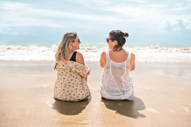 Two women sitting on the sandy beach facing the ocean in Pernambuco, Brazil.