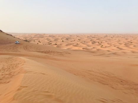 Explore the sweeping sand dunes of a remote desert with a lone 4x4 vehicle under clear skies.