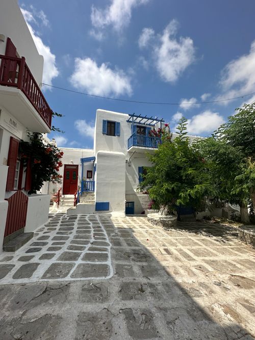 Free Explore a picturesque alley in Mykonos featuring traditional Cycladic architecture with blue shutters. Stock Photo