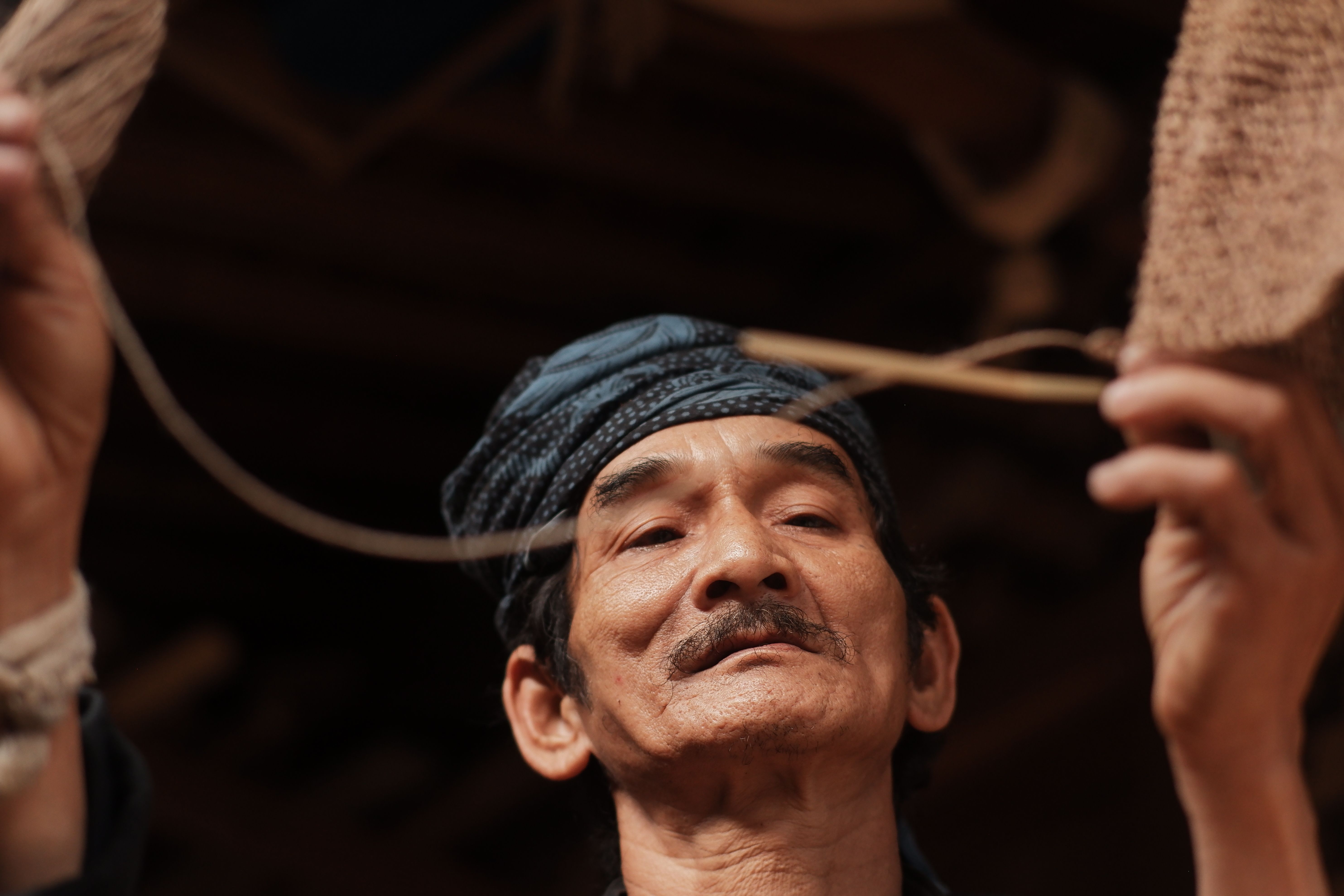 A close-up of an elderly Indonesian craftsman weaving a traditional basket, showcasing cultural heritage.