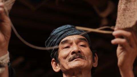 A close-up of an elderly Indonesian craftsman weaving a traditional basket, showcasing cultural heritage.