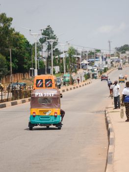 Vibrant street life in Jos, Nigeria with a colorful rickshaw on a sunny day.