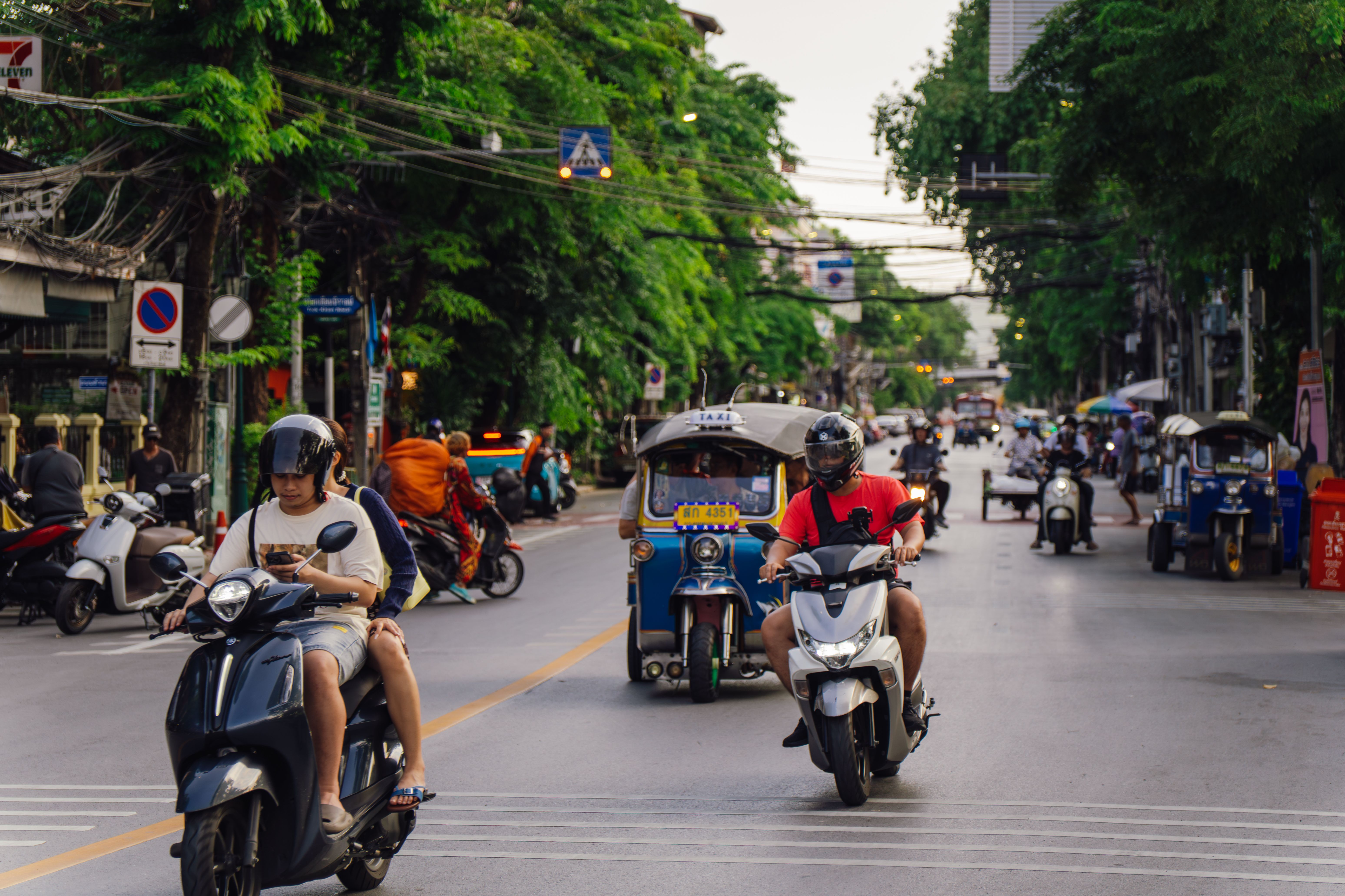 A vibrant Bangkok-metro street scene with motorbikes and tuk-tuks in motion during the day