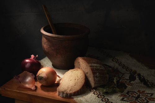 Free Artistic still life featuring bread, onions, and pottery on textured fabric. Stock Photo