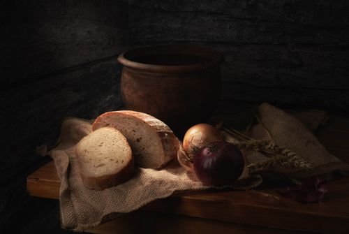 Free Moody still life featuring a rustic setting with bread, onions, and a clay pot on a wooden table. Stock Photo