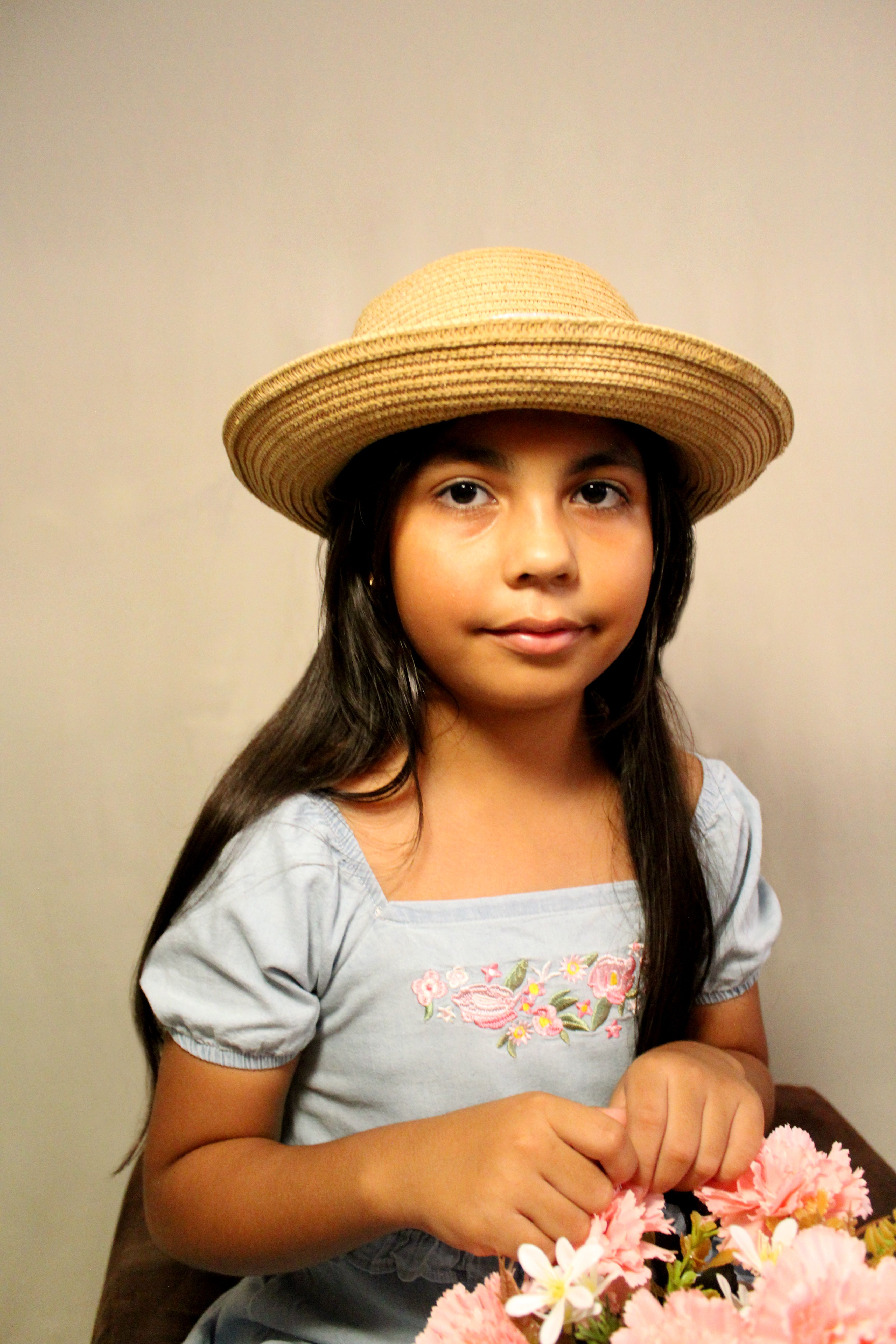 Portrait of a young girl wearing a straw hat, holding flowers, with a calm expression.