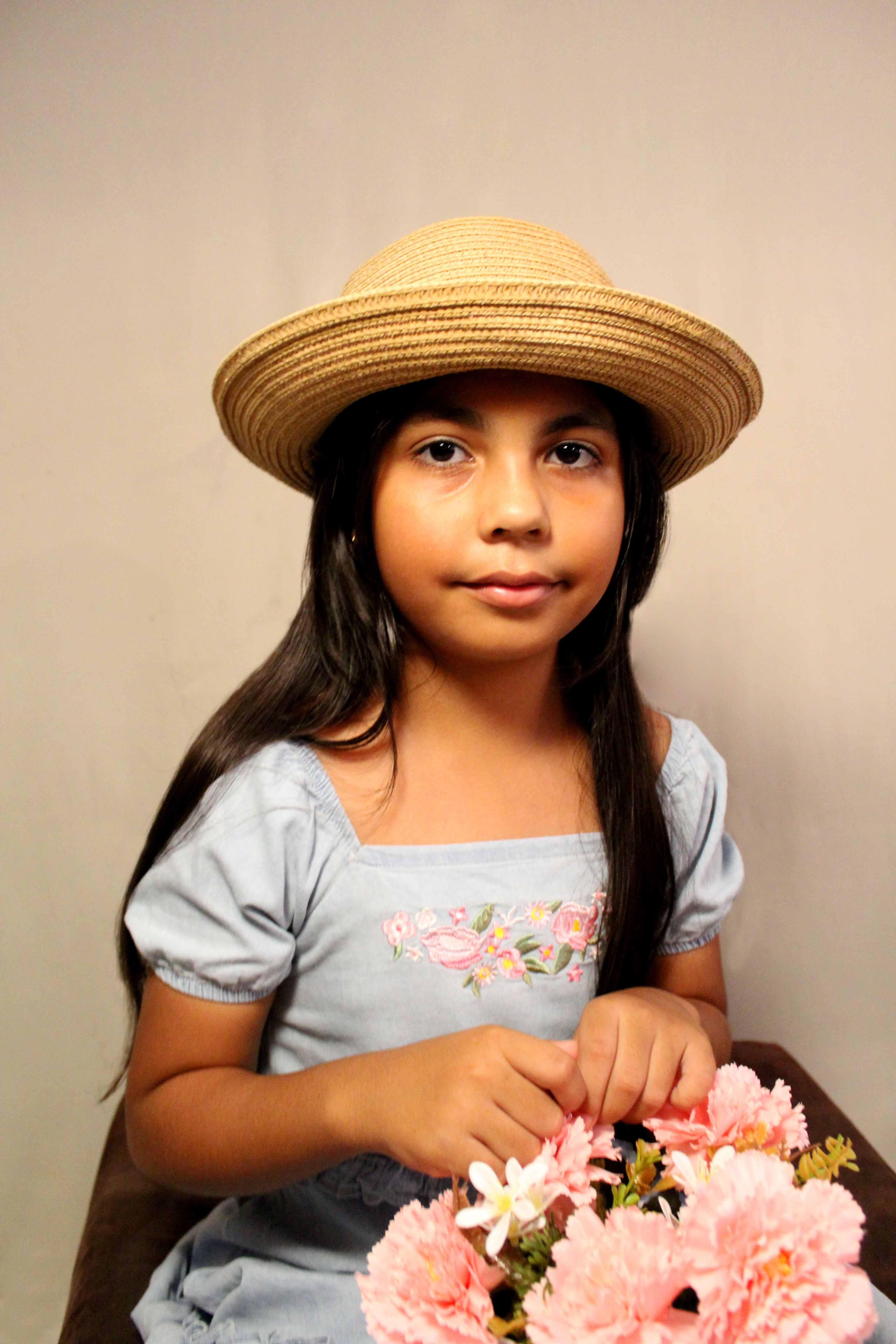 Charming portrait of a young girl in a straw hat holding a bouquet of pink flowers.