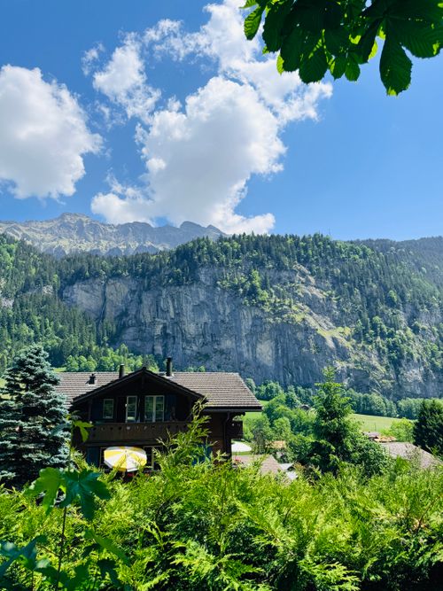 Free A picturesque Swiss chalet nestled in lush greenery with stunning mountain backdrop. Stock Photo