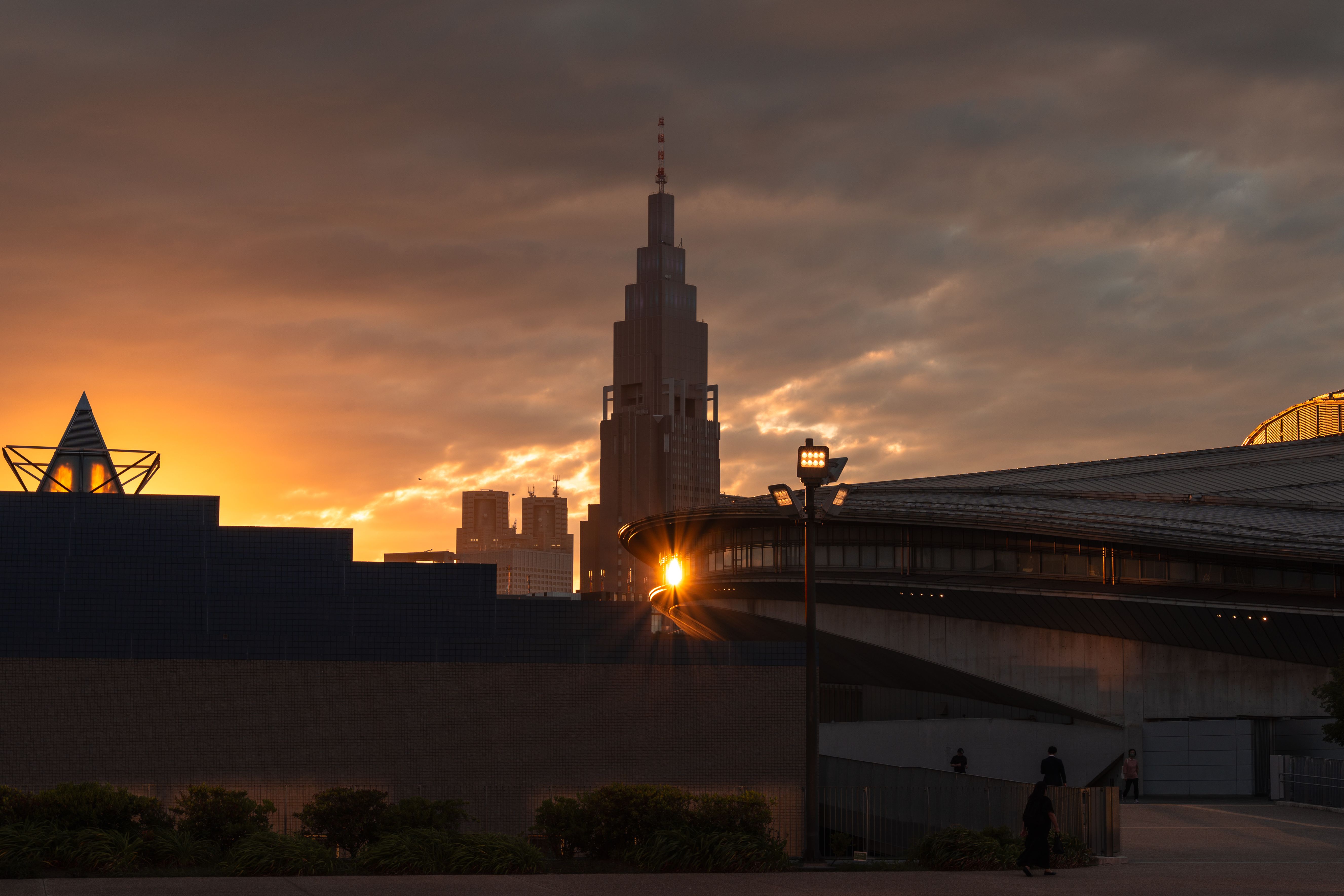 東京のスカイラインに沈む夕日のドラマチックな眺め。シルエットになった建物群と温かみのある色合いが印象的だ。
