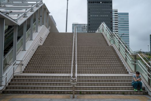 A person sitting on a staircase in an urban setting with modern architecture in Tokyo, Japan.
