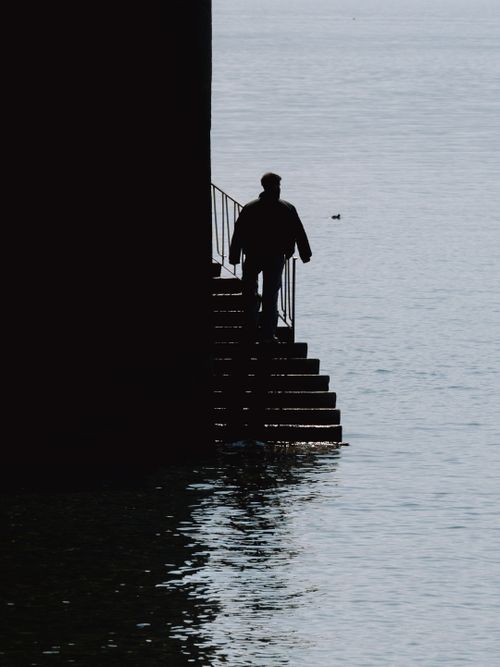 Free A dramatic silhouette of a man ascending a lakeside staircase at sunset. Stock Photo