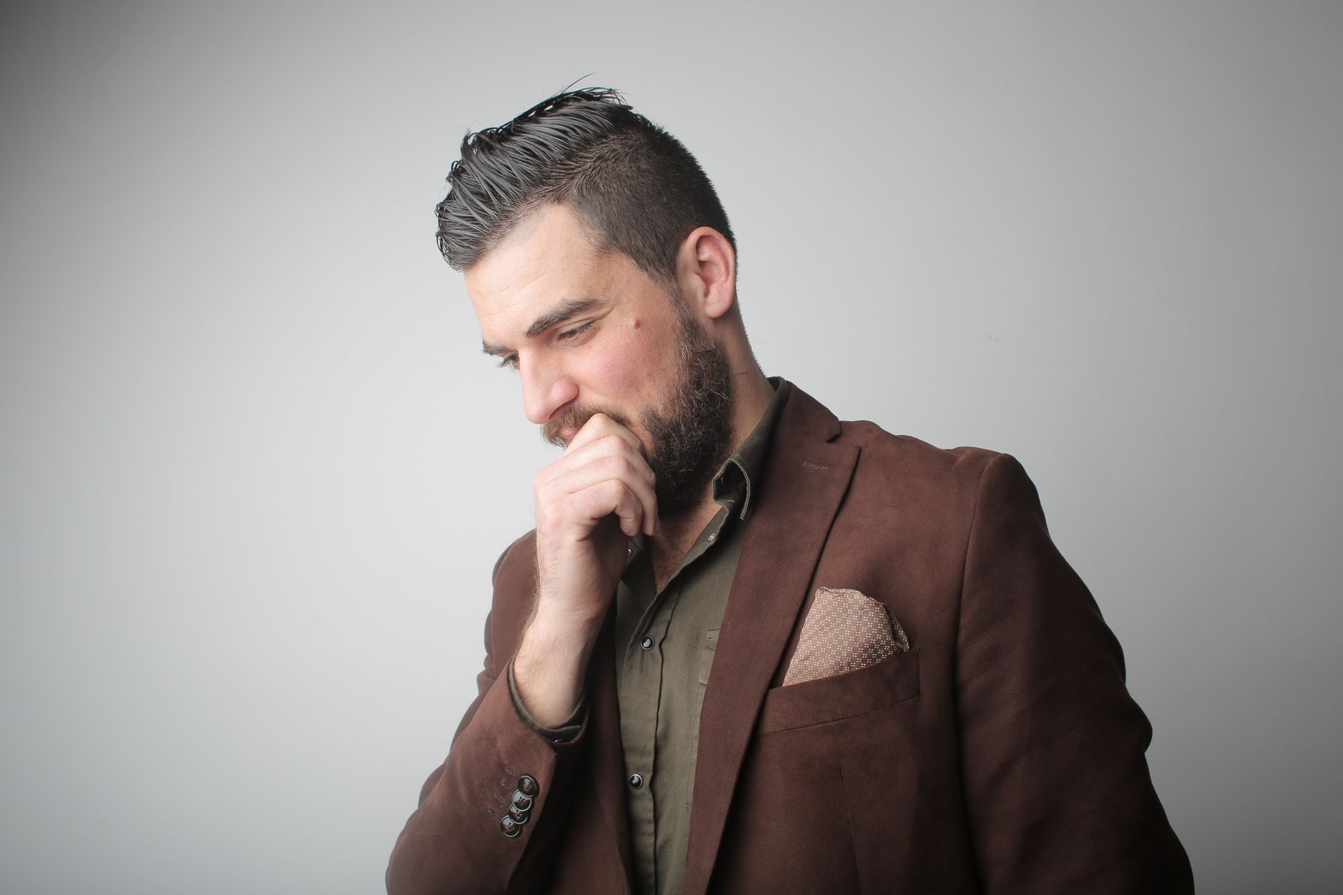 Thoughtful bearded man in brown suit contemplating in studio setting.