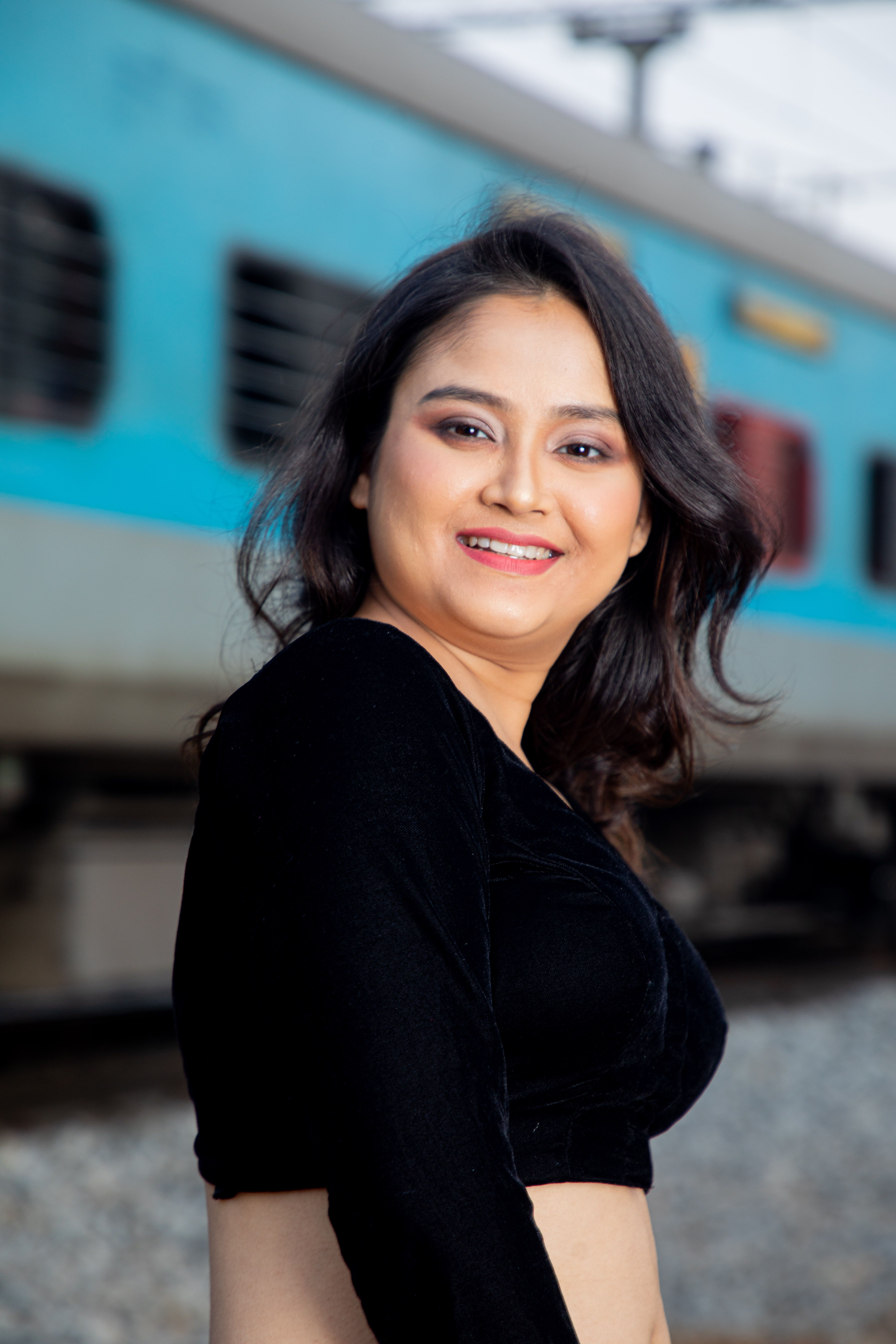 A stylish woman poses confidently outdoors with a moving train in the background.